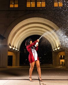 a woman in a red jacket spraying water on her face with a sprayer while standing under an archway at night