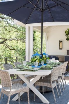 an outdoor dining table with blue and white chairs under an umbrella on a patio area