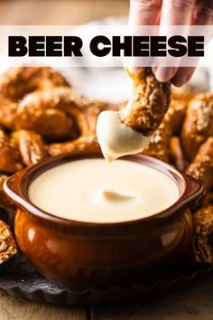 a hand dipping cheese into a bowl of dip with pretzels in the background