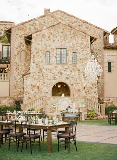 an outdoor dining area with tables and chairs in front of a large stone building that has a chandelier hanging from it's roof