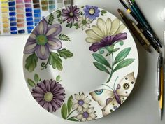 a plate with flowers painted on it next to paintbrushes and watercolors