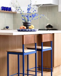 two blue stools sit in front of a kitchen island with flowers and fruit on it