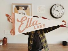 a person holding up a sign that says ella lane in front of a wall clock