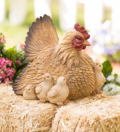 a mother chicken and her two chicks on hay bales with flowers in the background