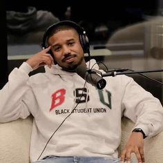 a man with headphones sitting in front of a microphone and wearing a white sweatshirt