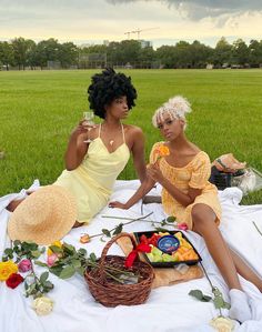 two women are sitting on a blanket in the grass eating fruit and having a picnic