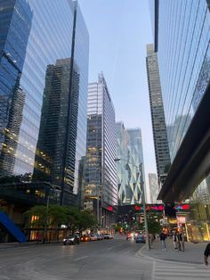 people are crossing the street in front of some very tall buildings and skyscrapers at dusk