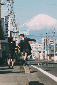 two people in kilts are walking down the street with a mountain in the background