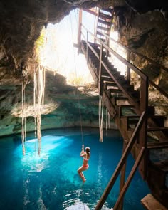 a woman hanging from a rope in the middle of a blue pool with stairs leading up to it