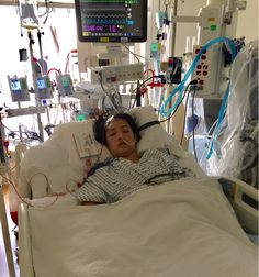 a woman laying in a hospital bed with headphones on and an iv monitor above her