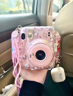 a person holding up a pink camera in the back seat of a car with hello kitty decorations on it