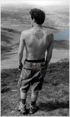 a man standing on top of a grass covered hill with a compass tattoo on his back