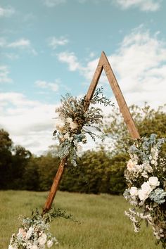 an arch decorated with flowers and greenery stands in the middle of a grassy field