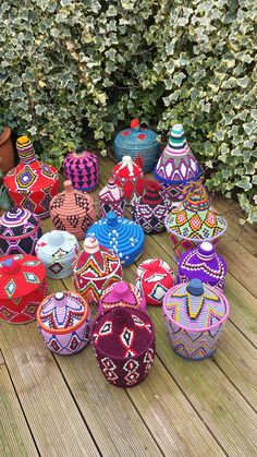 many colorful vases are sitting on a wooden deck next to some bushes and shrubbery