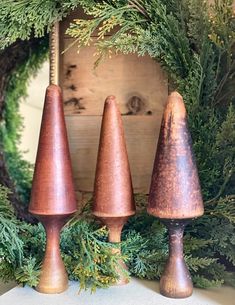 three copper candlesticks sitting on top of a table surrounded by greenery and wreath