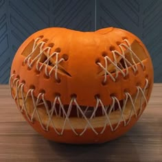 an orange pumpkin with white string wrapped around it's face and mouth, sitting on a wooden table