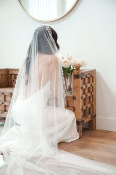 a woman in a wedding dress sitting on a bed with a veil over her head