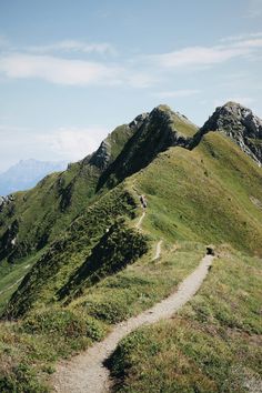 a path going up the side of a mountain with grass on both sides and mountains in the background