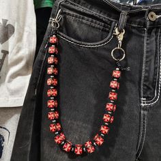 a red and black beaded necklace hanging from a pair of jeans