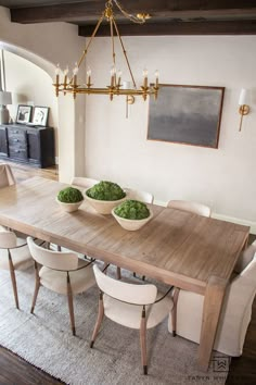 a dining room table with two bowls of green vegetables on it and chairs around it