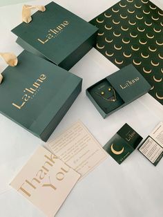 three green boxes with gold lettering on them sitting on a table next to cards and envelopes