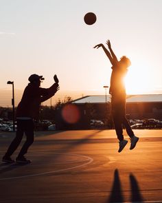 two people are playing basketball on an outdoor court with the sun setting in the background