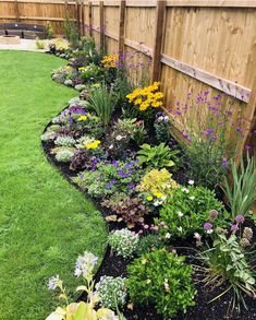 a garden filled with lots of flowers next to a wooden fence and green grass covered yard