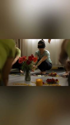 a woman arranging flowers on the floor in front of other people sitting down and looking at them