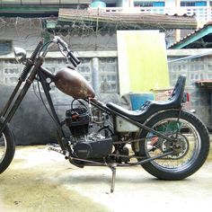 an old motorcycle is parked outside in the dirt near a building with no people on it