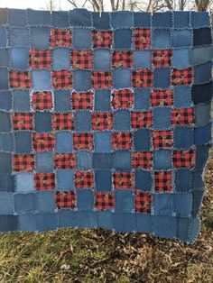 a blue quilt with red and black squares on it in the grass next to some trees