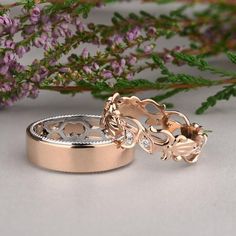 two wedding bands with leaves and hearts on them, sitting next to some purple flowers