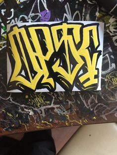 graffiti on the side of a wall with yellow and black letters that spell it out