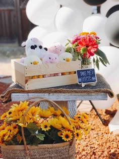 some stuffed animals are sitting in a basket on a table with sunflowers and flowers