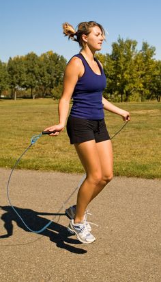 a woman is holding a jump rope and pulling it behind her on a road with trees in the background