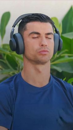 a man with headphones on his ears is looking at the camera while standing in front of some plants