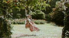 a woman sitting on a swing in the middle of a garden with trees and flowers