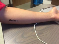 a person's arm with the word unless tattooed on it, sitting at a desk