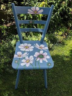 a blue chair with white daisies painted on it in front of some bushes and flowers