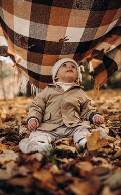 a baby is sitting under a blanket in the leaves on the ground with it's eyes closed