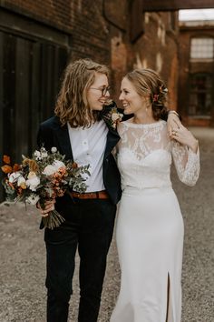 two people standing next to each other in front of a brick wall and holding flowers