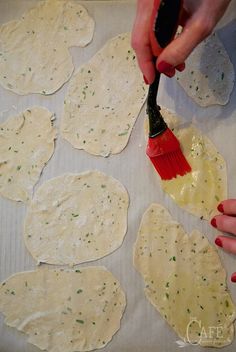 a person using a brush to make homemade pizzas on a sheet of baking paper