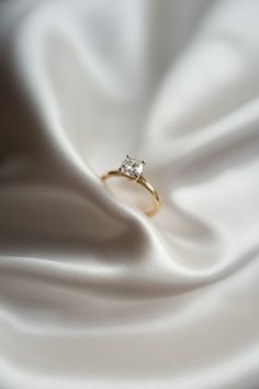 a diamond ring sitting on top of a white satin fabric, with the background visible