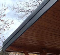 a wooden bench sitting under a roof next to a tree with no leaves on it