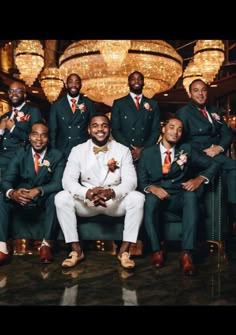 a group of men in green suits and ties posing for a photo with chandeliers behind them