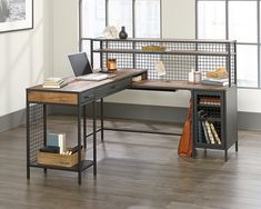 a desk with a laptop on it in front of two windows and a wooden floor