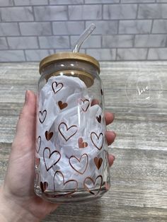 a hand holding a glass jar filled with white and brown heart patterned tissue paper in front of a brick wall