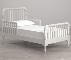 a small white bed sitting on top of a hard wood floor next to a gray wall