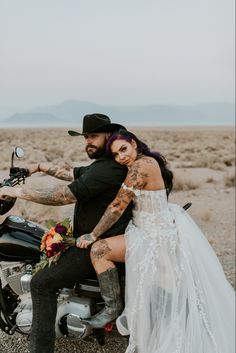 a man and woman sitting on a motorcycle in the middle of an open desert area