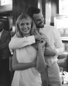 a man and woman are hugging each other in a black and white photo with people behind them