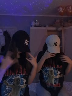 two young women sitting on the floor with baseball caps covering their faces in front of them